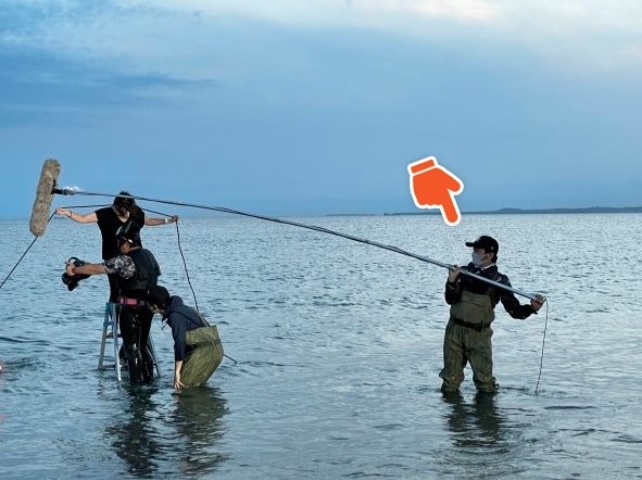 海で長い棒のついたマイクを掲げているあのひと、何してる？
